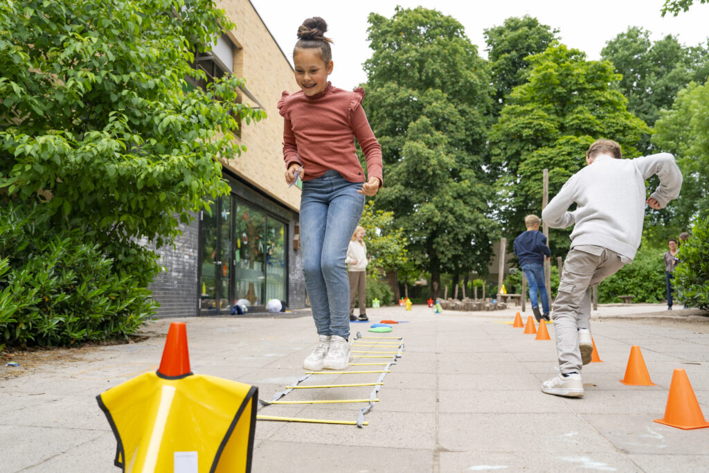Twee leerlingen sprinten met beweegkaartjes door een beweegparcours op het schoolplein.